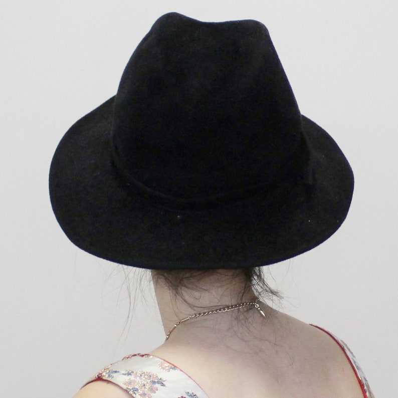 Puede incluir: Un sombrero fedora negro de ala ancha. El sombrero est&aacute; hecho de fieltro y tiene un acabado liso.