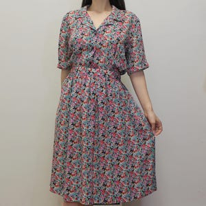 May include: A floral print dress with a collared neckline and short sleeves. The dress features a fitted waist and a knee-length skirt. The fabric is covered in a pattern of small flowers in shades of pink, blue, and black.