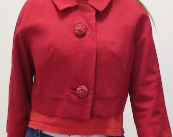 May include: A cropped red jacket with a rounded collar and three-quarter sleeves. The jacket has two textured buttons. The jacket is worn over a red top and blue jeans.