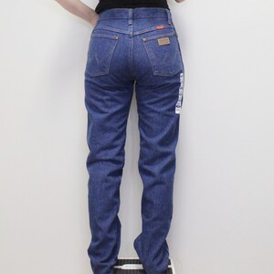 May include: A pair of blue denim jeans with a classic straight leg fit. The jeans have a high waist and a button fly closure. The back pockets have a stitched design and the brand name is visible on the back right pocket.