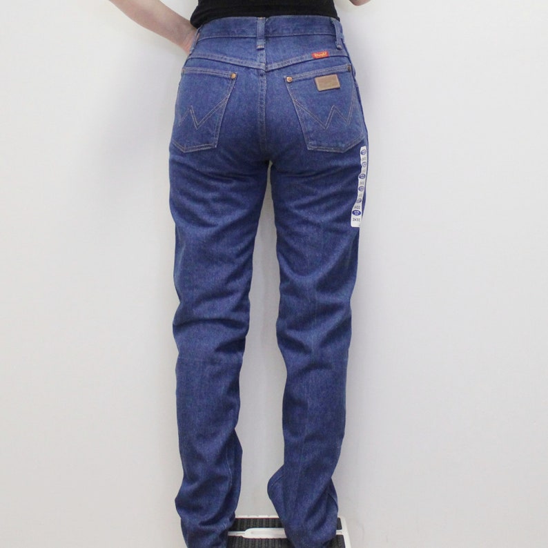 May include: A pair of blue denim jeans with a classic straight leg fit. The jeans have a high waist and a button fly closure. The back pockets have a stitched design and the brand name is visible on the back right pocket.