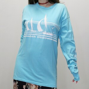 May include: A light blue long-sleeved t-shirt with a white graphic of sailboats and the text "SAN DIEGO".