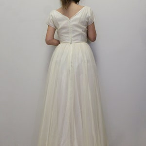 May include: A white, floor-length gown with a V-neckline and short sleeves. The dress has a zipper down the back and a gathered skirt.