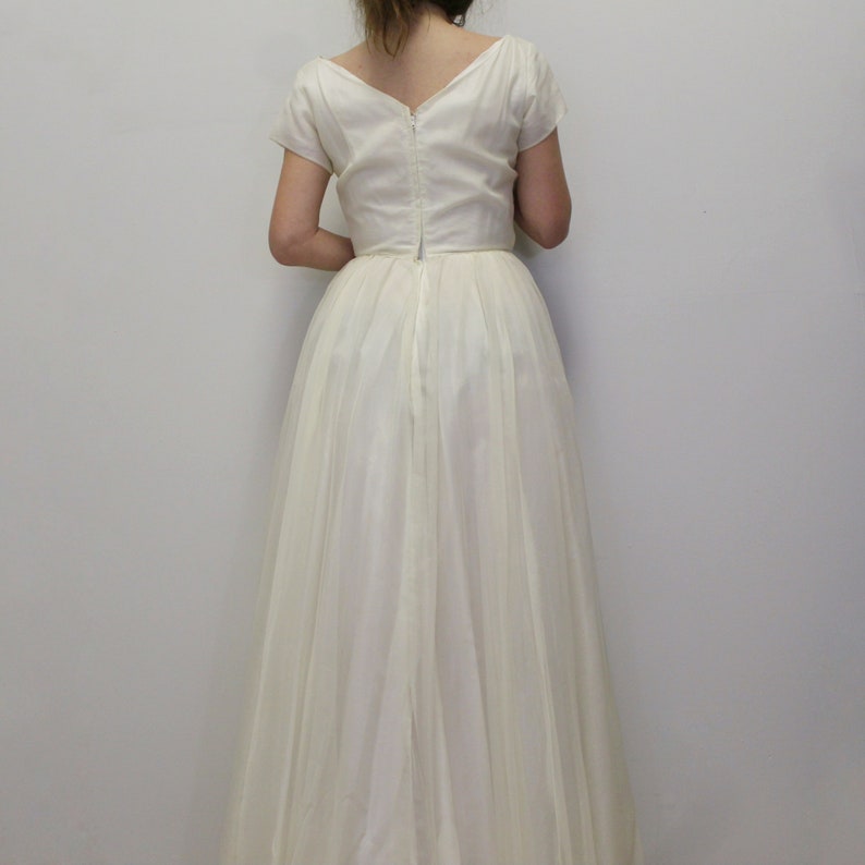May include: A white, floor-length gown with a V-neckline and short sleeves. The dress has a zipper down the back and a gathered skirt.