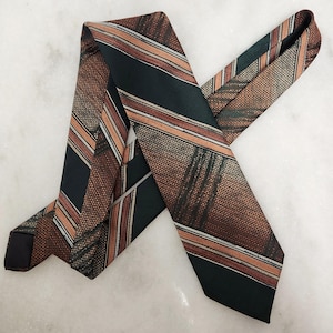 Peut inclure: Une cravate vintage à motifs rayés marron, vert et orange. La cravate a un aspect texturé et est présentée sur une surface blanche. Le design de la cravate présente des rayures diagonales et une extrémité pointue classique.
