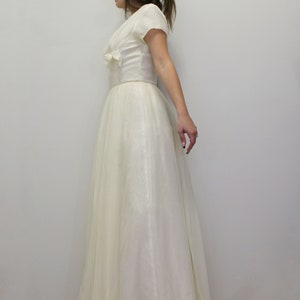 May include: A white vintage wedding dress with a fitted bodice and a full skirt. The dress has a V-neckline and short sleeves.