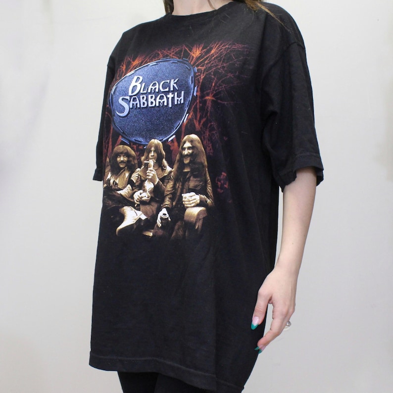 May include: Black t-shirt with a graphic of the band Black Sabbath. The graphic features the band members in a forest setting with a blue circle behind them that says "Black Sabbath".