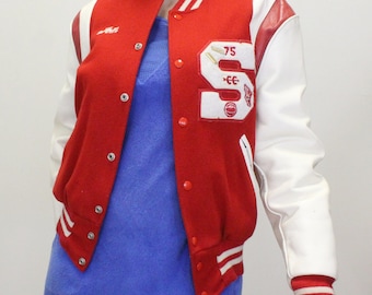 Op de afbeelding: Rood en wit varsity jack met een grote witte letter "S" aan de linkerkant. De letter heeft het nummer "75" erboven en een klein rood-wit ontwerp eronder. Het jack heeft een witte leren mouw en een rode wollen mouw.