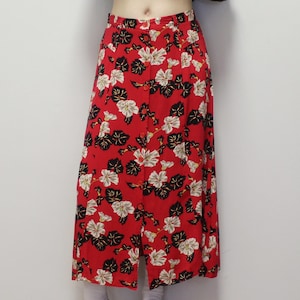 May include: A red, knee-length skirt with a floral design. The skirt has a button-down front and features white and black flowers with green leaves. The skirt has a front slit.