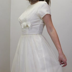 May include: A white vintage dress with a bow at the neckline and a full skirt.