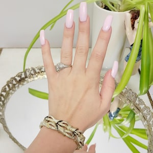 May include: A gold-toned bracelet with a braided design. The bracelet is on a person's wrist. The person is wearing a ring on their finger.