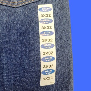 May include: A blue denim fabric with a white tag attached. The tag has multiple labels that read "Slim Fit" and "3X32".