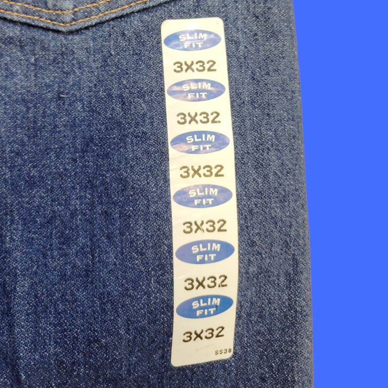 May include: A blue denim fabric with a white tag attached. The tag has multiple labels that read "Slim Fit" and "3X32".