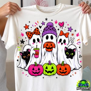 May include: A white t-shirt featuring a graphic of three white ghosts and two black cats. The ghosts wear a polka dot bow, a purple leopard print beanie, and a red bow. They hold a pumpkin bucket and a pink drink. Three jack-o'-lanterns sit below.