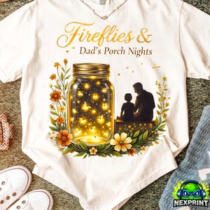 Può includere: T-shirt bianca con una grafica raffigurante un barattolo pieno di lucciole luminose, una candela e la silhouette di un genitore e un bambino. Il testo recita "Fireflies & Dad's Porch Nights". Accenti floreali circondano il barattolo.