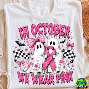 May include: A white t-shirt featuring a graphic of two ghosts with pink floral patterns. One ghost wears a pink gingham bow, and the other holds a pink awareness ribbon. The text reads IN OCTOBER WE WEAR PINK, surrounded by bats and checkered flags.