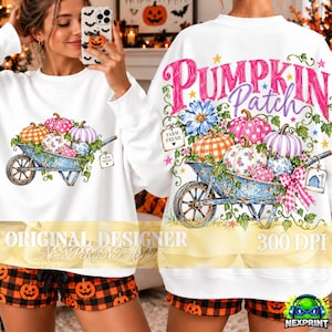 Puede incluir: Una sudadera blanca de manga larga con un gráfico de una carretilla azul llena de calabazas coloridas con patrones, enredaderas y flores. El texto PUMPKIN Patch está impreso en rosa y morado sobre la carretilla con una etiqueta Farm Fresh.
