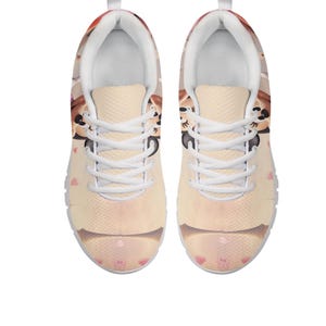 K&ouml;nnte beinhalten: Paar Sportschuhe mit einem Cartoon-Katzen-Design. Die Schuhe haben eine hellbeige Grundfarbe mit einem sich wiederholenden Muster aus rosa Herzen und Katzenk&ouml;pfen. Wei&szlig;e Schn&uuml;rsenkel und Sohlen.