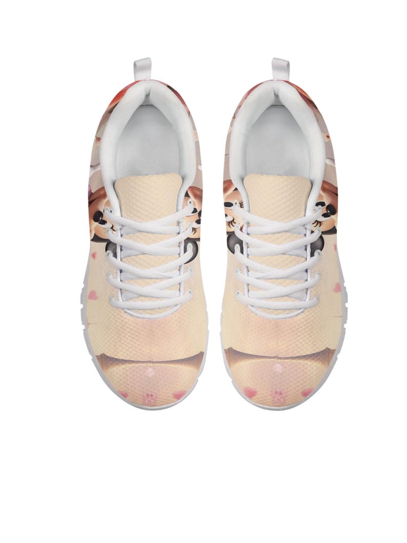 K&ouml;nnte beinhalten: Paar Sportschuhe mit einem Cartoon-Katzen-Design. Die Schuhe haben eine hellbeige Grundfarbe mit einem sich wiederholenden Muster aus rosa Herzen und Katzenk&ouml;pfen. Wei&szlig;e Schn&uuml;rsenkel und Sohlen.