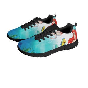 May include: Pair of trainers with a colourful aquatic design. The shoes feature a blue and white background with cartoon illustrations of a mermaid, a yellow fish, and other characters. The shoes have black laces and soles.