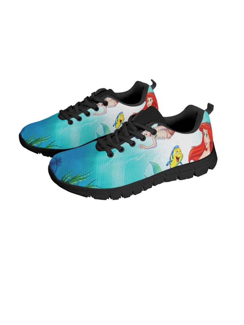 May include: Pair of trainers with a colourful aquatic design. The shoes feature a blue and white background with cartoon illustrations of a mermaid, a yellow fish, and other characters. The shoes have black laces and soles.