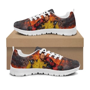 Può includere: Un paio di scarpe da ginnastica con suola bianca con una grafica colorata di personaggi dei fumetti su uno sfondo infuocato. Le scarpe hanno lacci bianchi e un tallone nero. Le scarpe sono esposte su una scatola di cartone marrone.