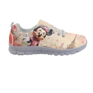 K&ouml;nnte beinhalten: Ein hellfarbener Sportschuh mit einem Minnie-Mouse-Motiv. Der Schuh hat eine graue Sohle, Schn&uuml;rsenkel und Zierleisten. Das Design umfasst eine rosa Schleife, Herzen und ein Cartoon-Bild von Minnie Mouse.