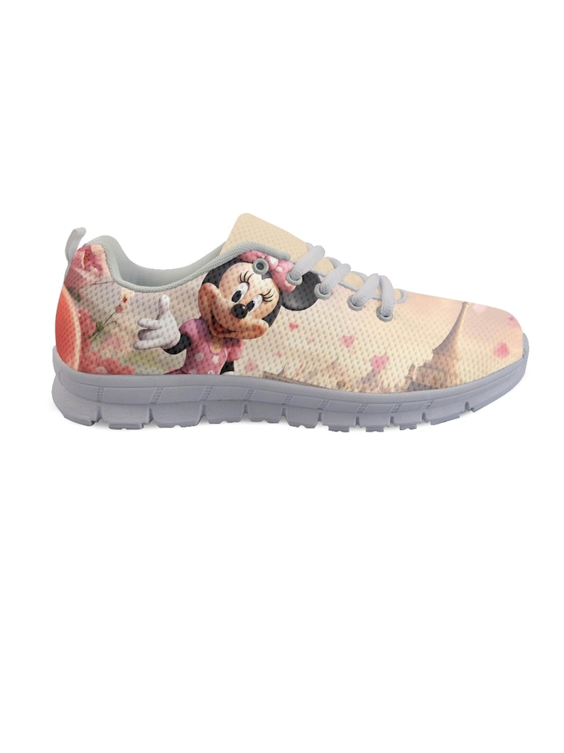 K&ouml;nnte beinhalten: Ein hellfarbener Sportschuh mit einem Minnie-Mouse-Motiv. Der Schuh hat eine graue Sohle, Schn&uuml;rsenkel und Zierleisten. Das Design umfasst eine rosa Schleife, Herzen und ein Cartoon-Bild von Minnie Mouse.