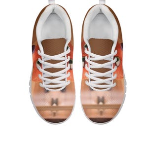 May include: A pair of trainers with a cartoon fox face design. The shoes have white laces, a white sole, and a brown tongue. The fox's face is orange and white, with green eyes.