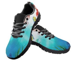 May include: A pair of trainers with a blue and teal ocean design. The shoes feature a cartoon mermaid and fish, with black soles and grey laces. The design includes green seaweed and blue starfish.