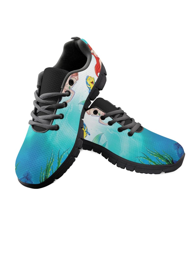 May include: A pair of trainers with a blue and teal ocean design. The shoes feature a cartoon mermaid and fish, with black soles and grey laces. The design includes green seaweed and blue starfish.