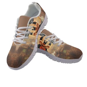 Pu&ograve; includere: Un paio di scarpe sportive con un'immagine a cartoni animati di Topolino. Le scarpe hanno una combinazione di colori marrone e bianco, con lacci e suole bianche. Il design include un'illustrazione dettagliata di Topolino sui lati.