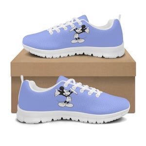 May include: Pale blue athletic trainers with white soles and laces. The trainers feature a black and white graphic of Mickey Mouse on the side. The trainers are displayed on a brown cardboard box.