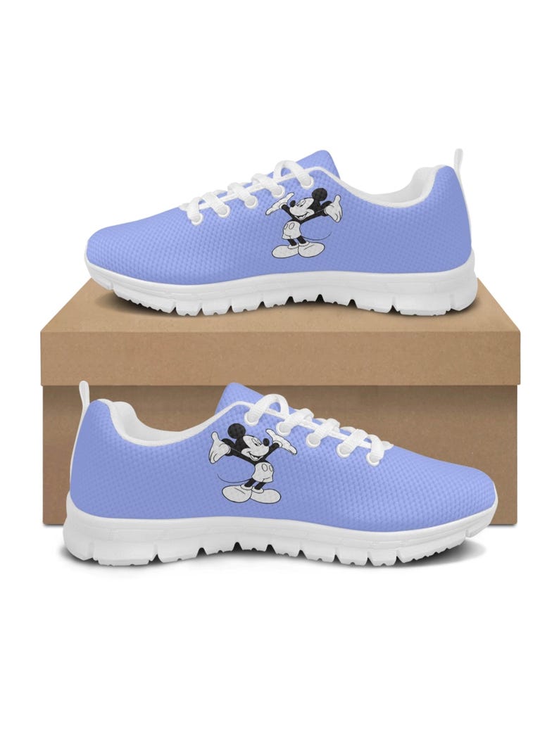 May include: Pale blue athletic trainers with white soles and laces. The trainers feature a black and white graphic of Mickey Mouse on the side. The trainers are displayed on a brown cardboard box.