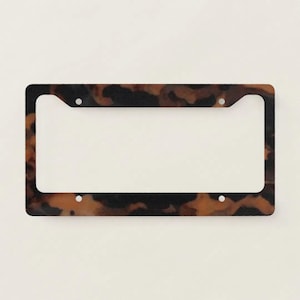 May include: A rectangular license plate frame with a tortoiseshell pattern in shades of brown and black. The frame has four mounting holes and a large central opening for the license plate.