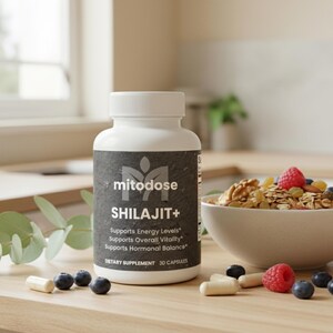 May include: A white bottle of "mitodose SHILAJIT+" dietary supplement with a black label. The label includes text about supporting energy levels, overall vitality, and hormonal balance. Capsules, blueberries, and raspberries are scattered on the wooden surface.
