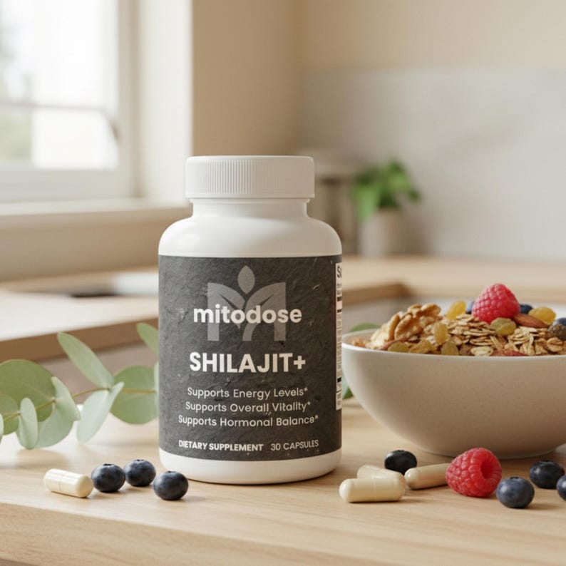 May include: A white bottle of "mitodose SHILAJIT+" dietary supplement with a black label. The label includes text about supporting energy levels, overall vitality, and hormonal balance. Capsules, blueberries, and raspberries are scattered on the wooden surface.