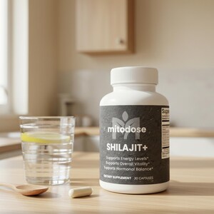 May include: A white bottle of "mitodose SHILAJIT+" dietary supplement with a gray label, a glass of water with a lemon slice, a wooden spoon, and a capsule on a wooden surface. The label states the supplement supports energy levels, overall vitality, and hormonal balance.