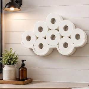 May include: A white wall-mounted toilet paper holder shaped like a cloud, holding eight rolls of white toilet paper. The holder is positioned on a white paneled wall. The text CONTEMPORARY FARMHOUSE is visible at the bottom of the image.