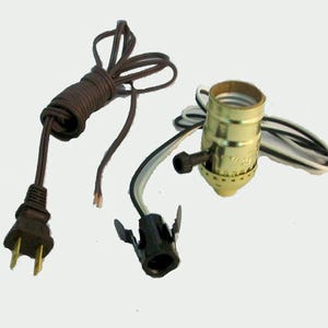 May include: A collection of electrical components for a lamp, including a brown power cord with a black plug, a brass-colored lamp socket, and a black socket connector. The wires are black, white, and copper-colored.