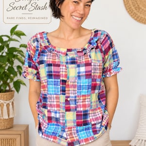 May include: A short-sleeved blouse featuring a multi-colored patchwork plaid pattern in shades of blue, red, yellow, and white. The blouse has a square neckline with a ruffled trim, short puffed sleeves with ruffled cuffs, and a front button closure.