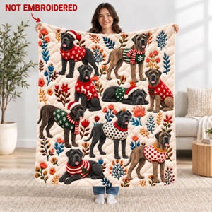 Könnte beinhalten: Eine cremefarbene, gesteppte Wohndecke mit einem wiederkehrenden Muster aus schwarzen Hunden, die verschiedene weihnachtliche Pullover und Mützen tragen, durchsetzt mit bunten Blumenmotiven. Der Text NOT EMBROIDERED steht oben links in Rot.
