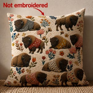 May include: A square throw pillow with a cream-colored textured background featuring a repeating pattern of brown bison wearing various patterned sweaters and colorful floral accents. The text "Not embroidered" is printed at the top.