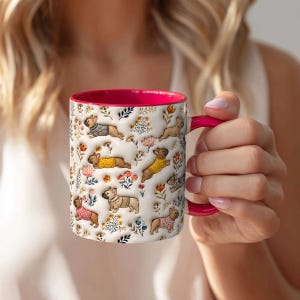 May include: A white ceramic mug with a vibrant hot pink interior and handle. The exterior features a repeating pattern of small French bulldogs wearing colorful sweaters, interspersed with various delicate floral illustrations in autumn tones.