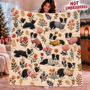 May include: A cream-colored throw blanket featuring a repeating pattern of black and white Border Collie dogs wearing various sweaters, interspersed with colorful floral illustrations. The text NOT EMBROIDERED is printed in red.