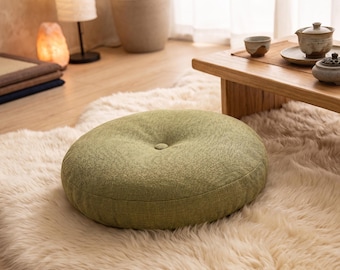 Cojín redondo verde para el suelo, confeccionado en tejido texturizado para crear un espacio zen y relajante.