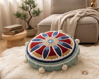 Cojín redondo de estilo bohemio con coloridos estampados florales y borlas.