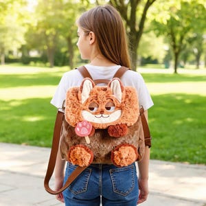 May include: A novelty backpack in the shape of a fox, with a plush, textured exterior in shades of brown and orange. It has brown leather straps and a smiling fox face. The backpack is worn by a person in a white t-shirt and blue jeans.