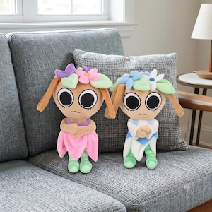 May include: Two plush dolls with large black eyes and flower-shaped headpieces. The left doll wears a purple top and pink skirt, while the right doll wears a white and blue outfit. Both have light brown skin, long ears, and green striped legs.