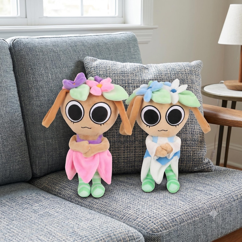 May include: Two plush dolls with large black eyes and flower-shaped headpieces. The left doll wears a purple top and pink skirt, while the right doll wears a white and blue outfit. Both have light brown skin, long ears, and green striped legs.